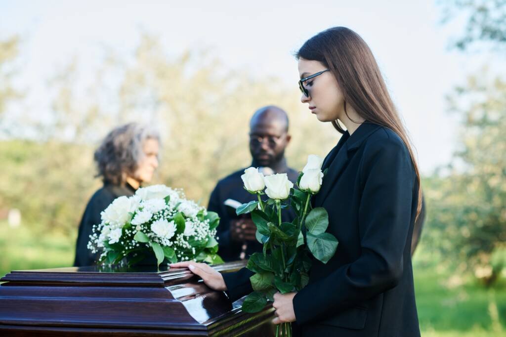 Side view of young mourning woman with bunch of white roses