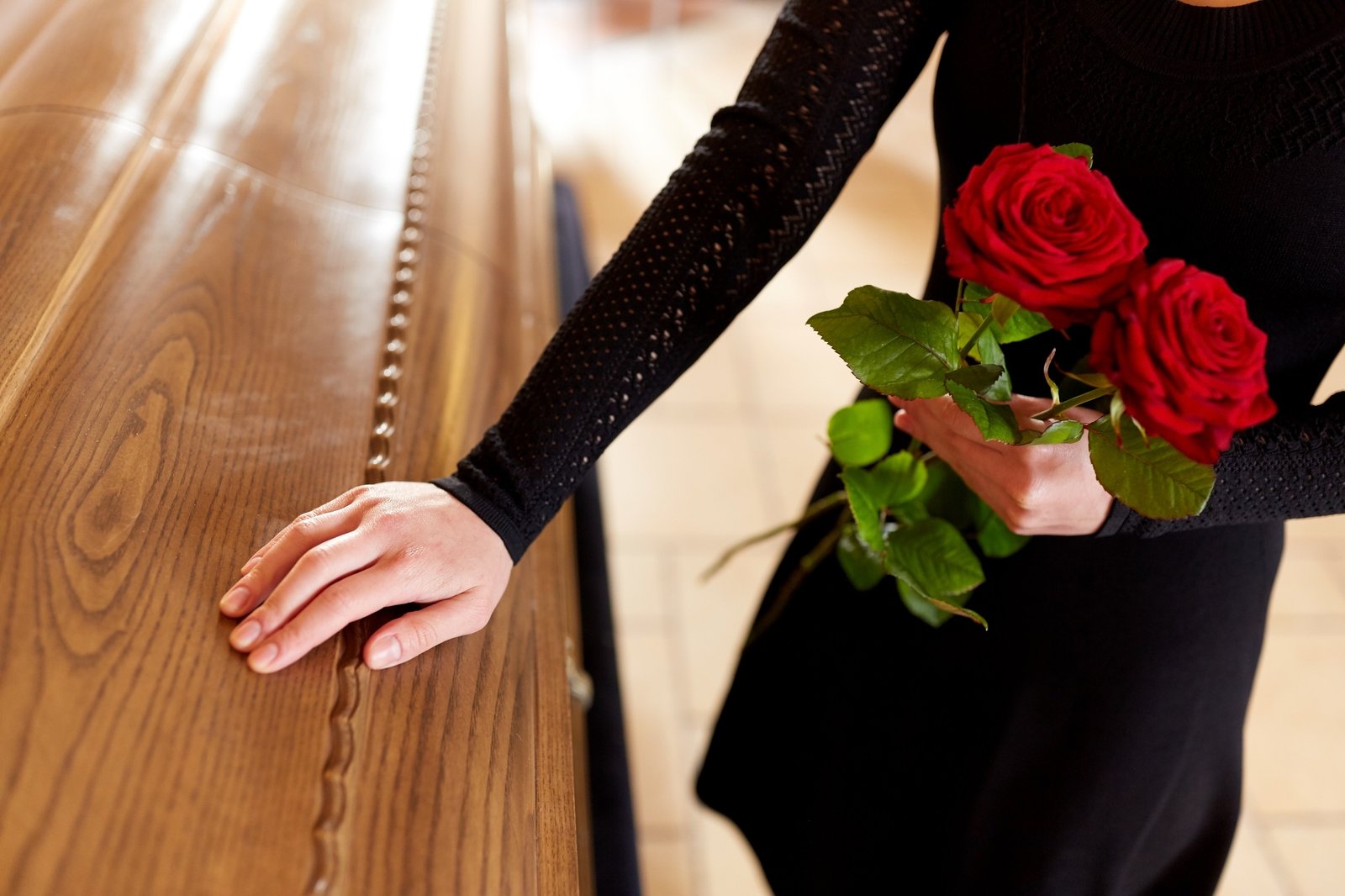 woman with red roses and coffin at funeral